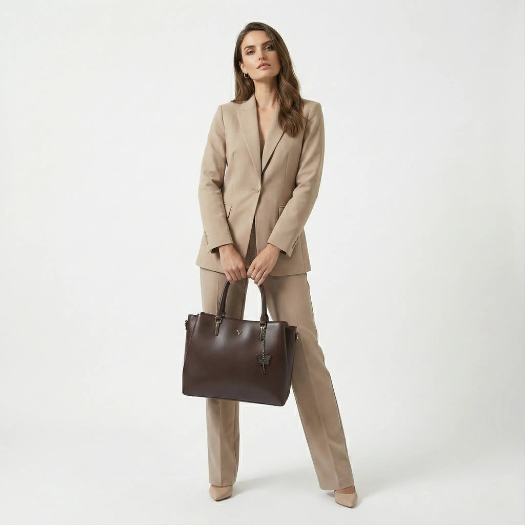 Woman in beige pantsuit holding a large brown leather handbag, modern fashion look