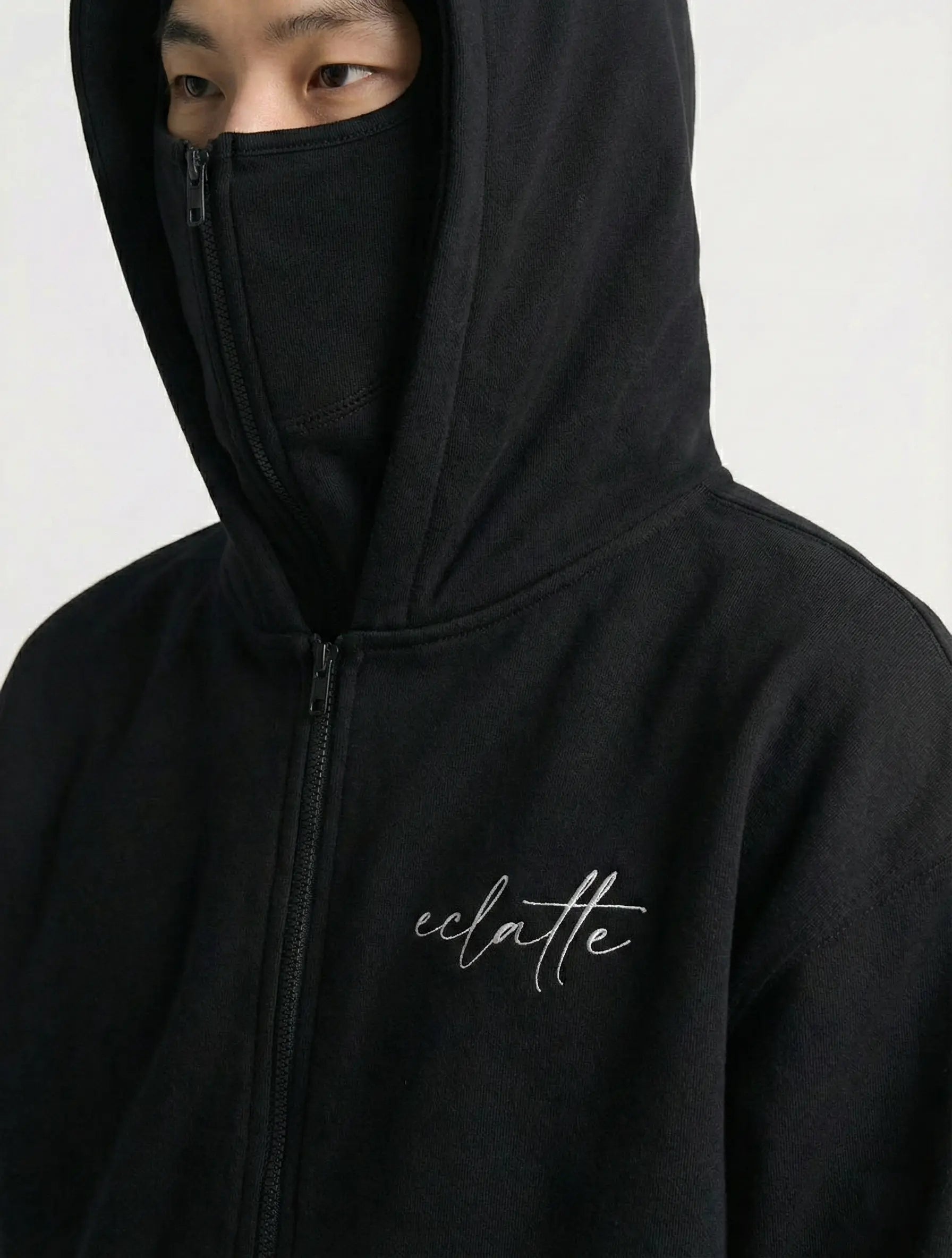 Model in black zip-up hoodie with concealed face and 'eclatte' script logo on chest