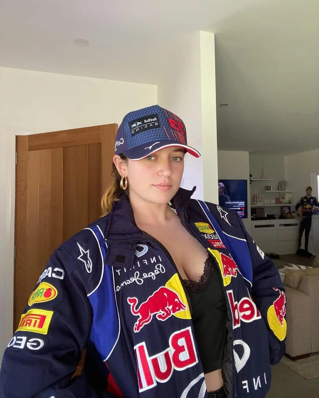Woman wearing Red Bull Racing jacket and cap in a modern living room, Gen Z streetwear style