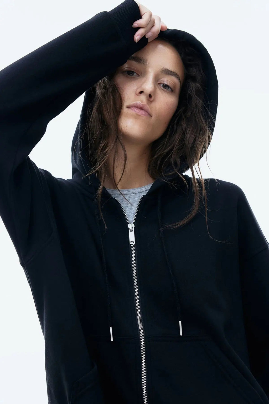 Woman wearing black zip-up hoodie with hood up, casual streetwear fashion