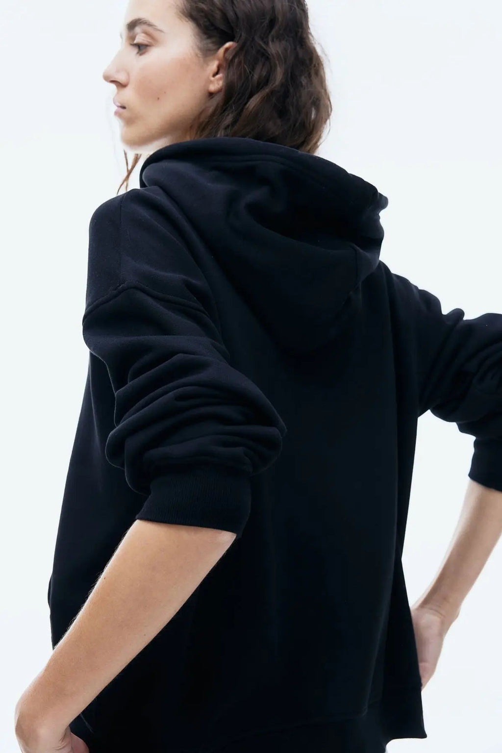 Side view of woman wearing a black zip-up hoodie with hood, casual streetwear style